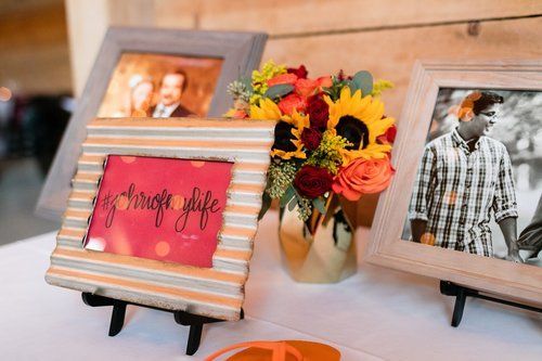 Framed photos and a small vase of orange and yellow flowers on a table