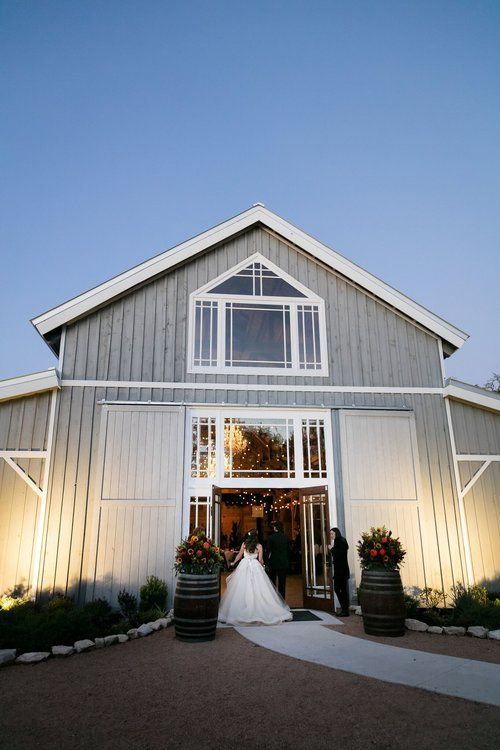 White barn-style wedding venue at dusk with a bride standing in the open doorway