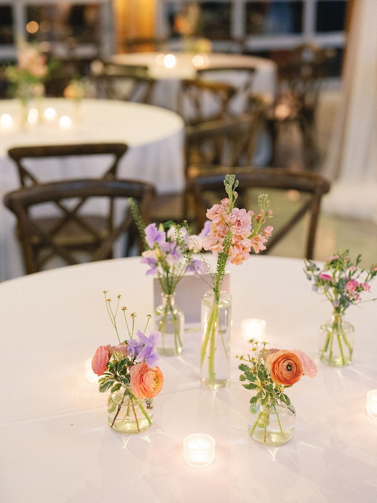 Small flower vases with pink, purple, and orange blooms on a round table in a softly lit café