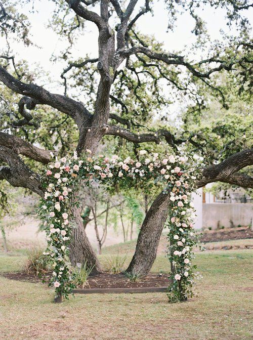Flower-decorated archway under a large tree in a grassy outdoor setting