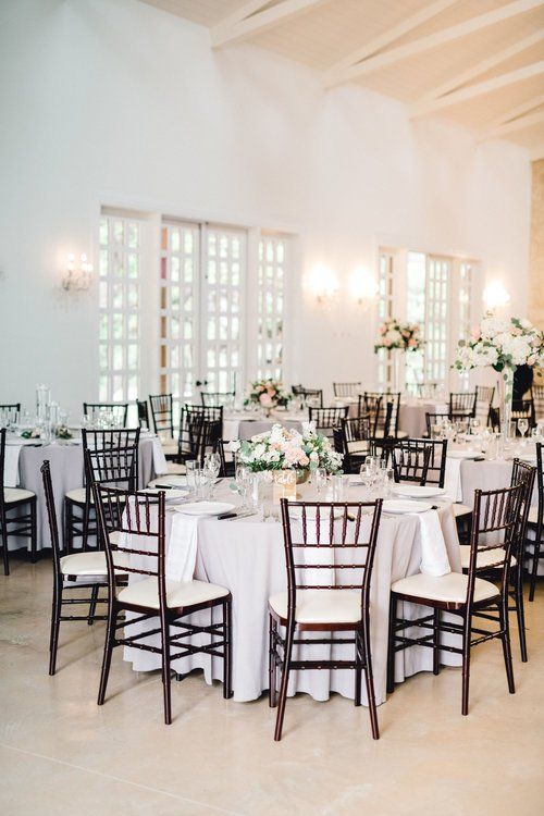 Elegant banquet hall with round white-clothed tables, dark chairs, and floral centerpieces under high ceilings