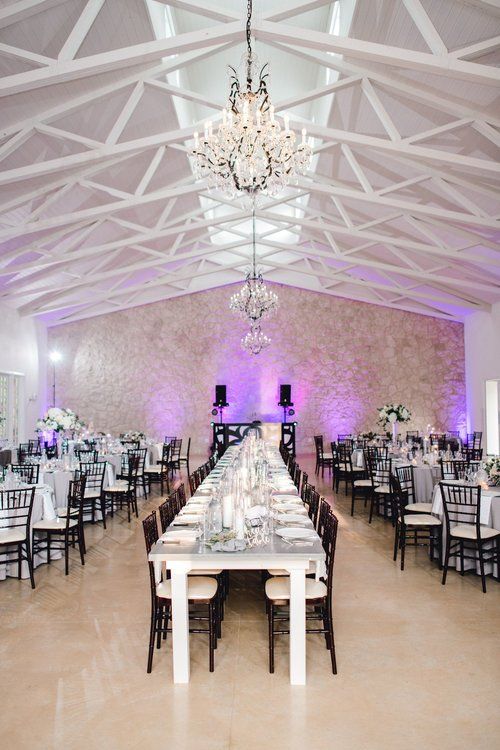 Elegant banquet hall with chandeliers, white vaulted ceiling, and long mirrored dining table with black chairs