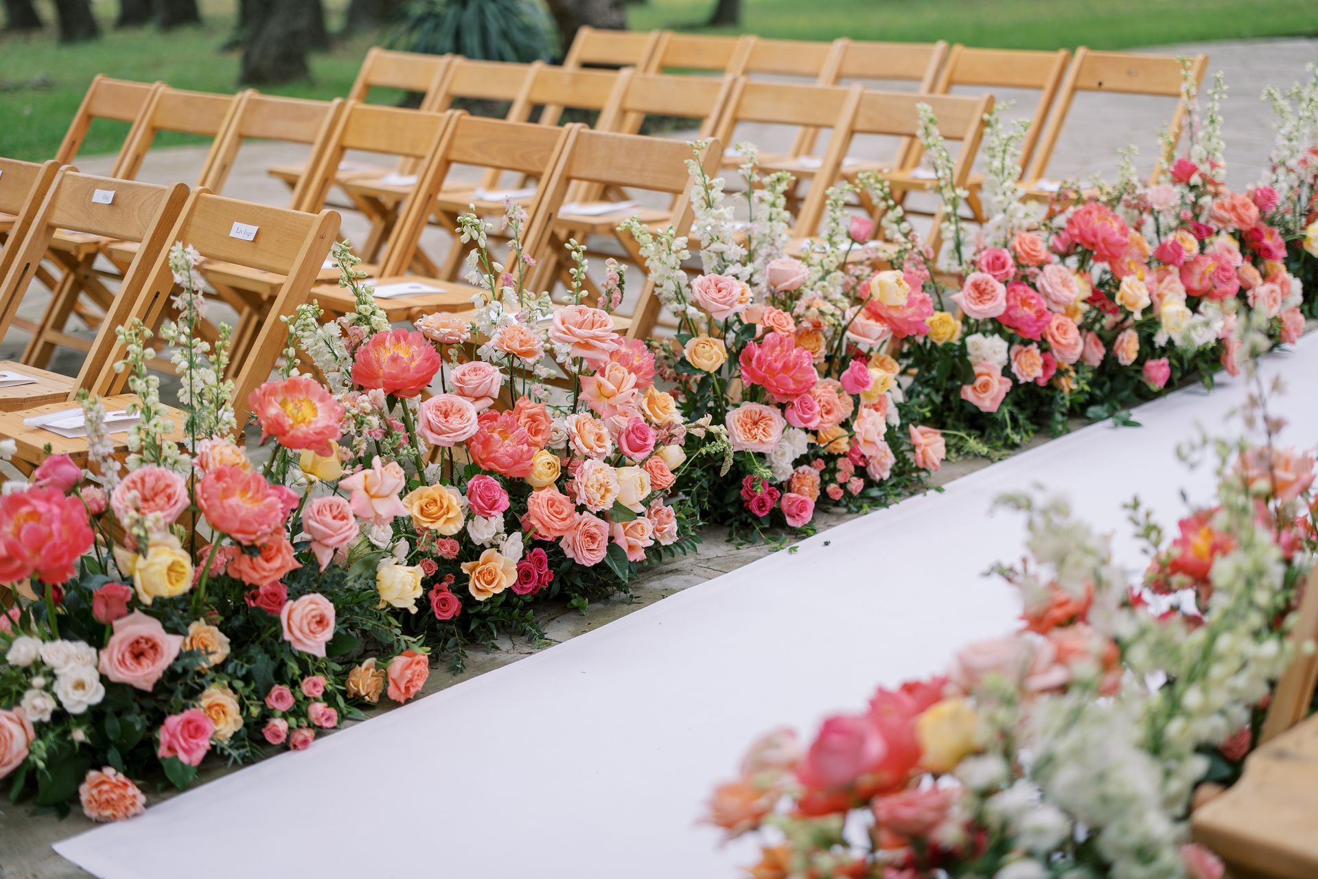 Floral-lined white aisle with wooden chairs for an outdoor wedding ceremony