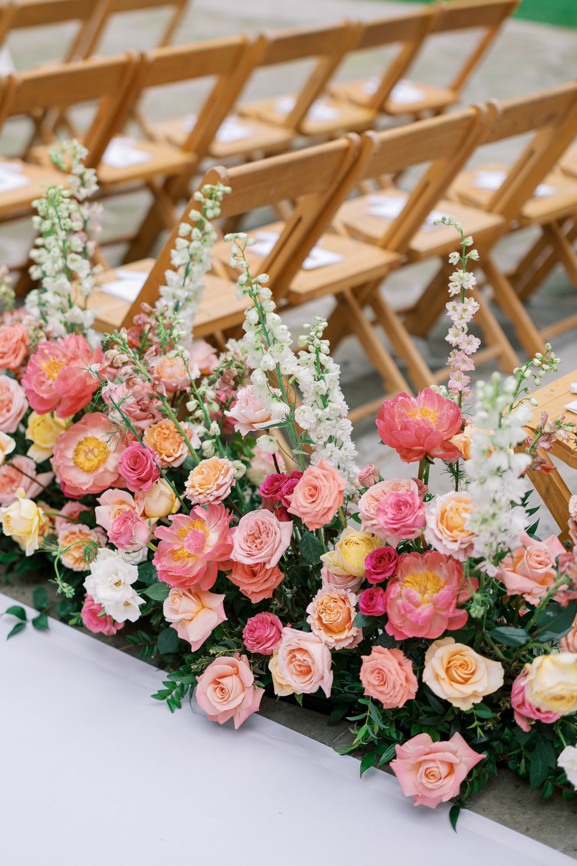 Pink and peach floral arrangement in front of rows of wooden chairs at an outdoor event