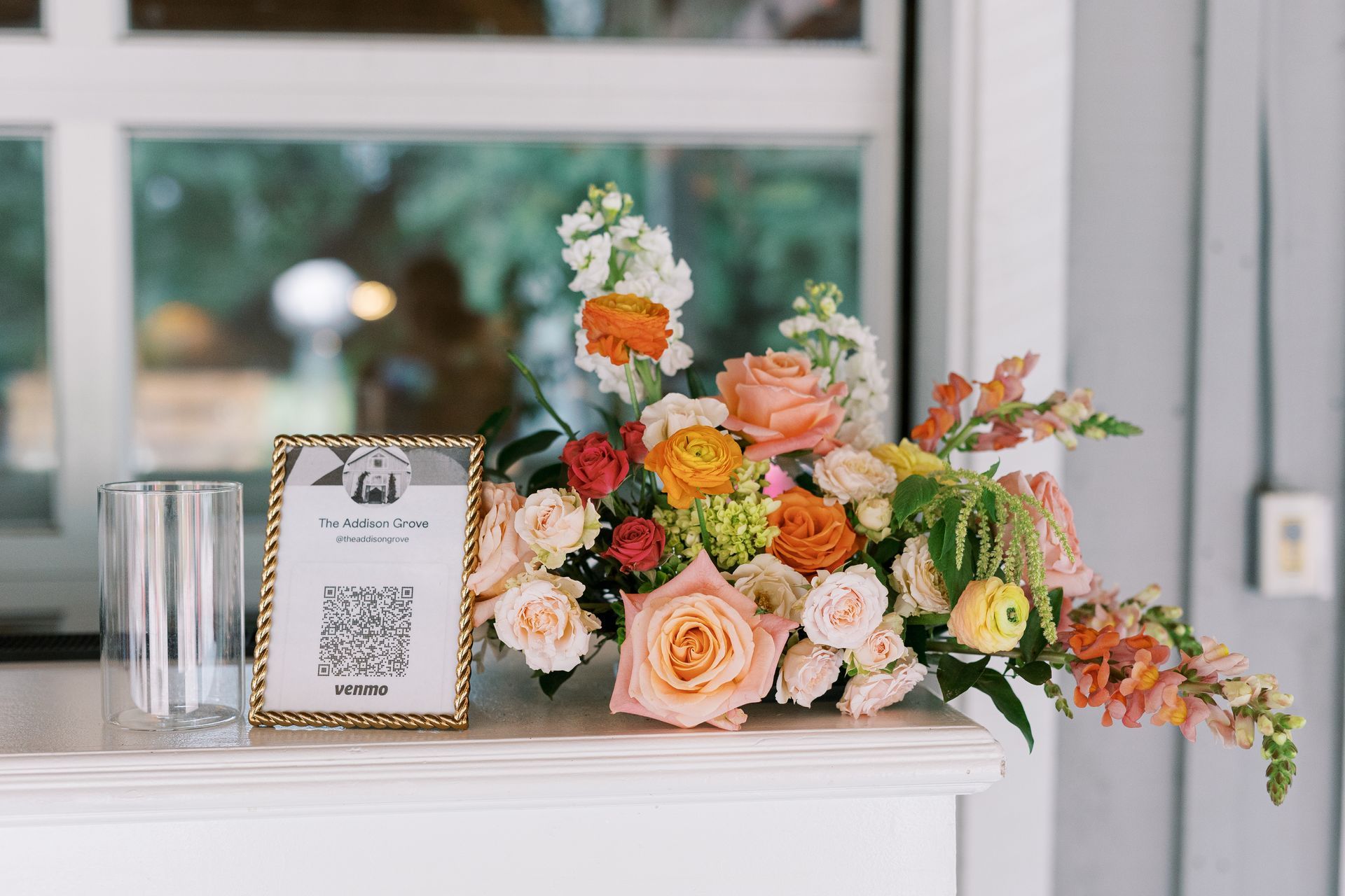 Orange and peach floral arrangement beside a framed table sign on a white mantel