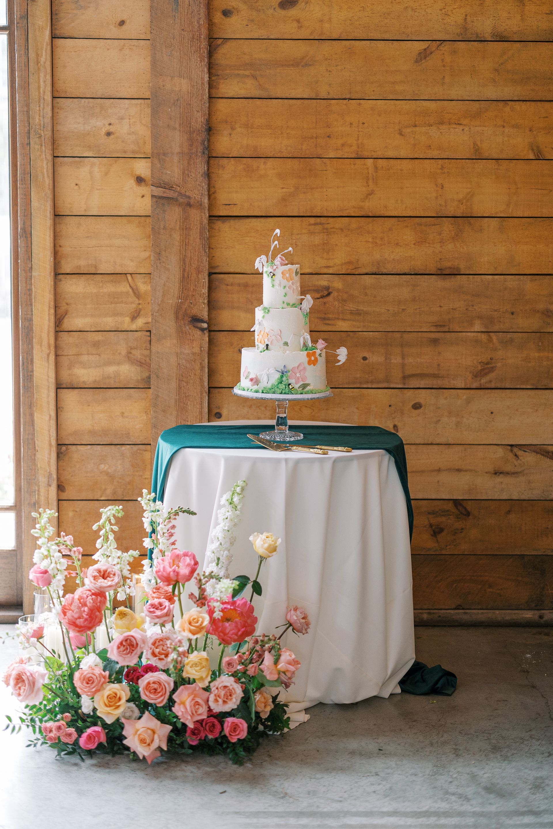 Wedding cake and pink floral arrangement on a table against a wooden wall