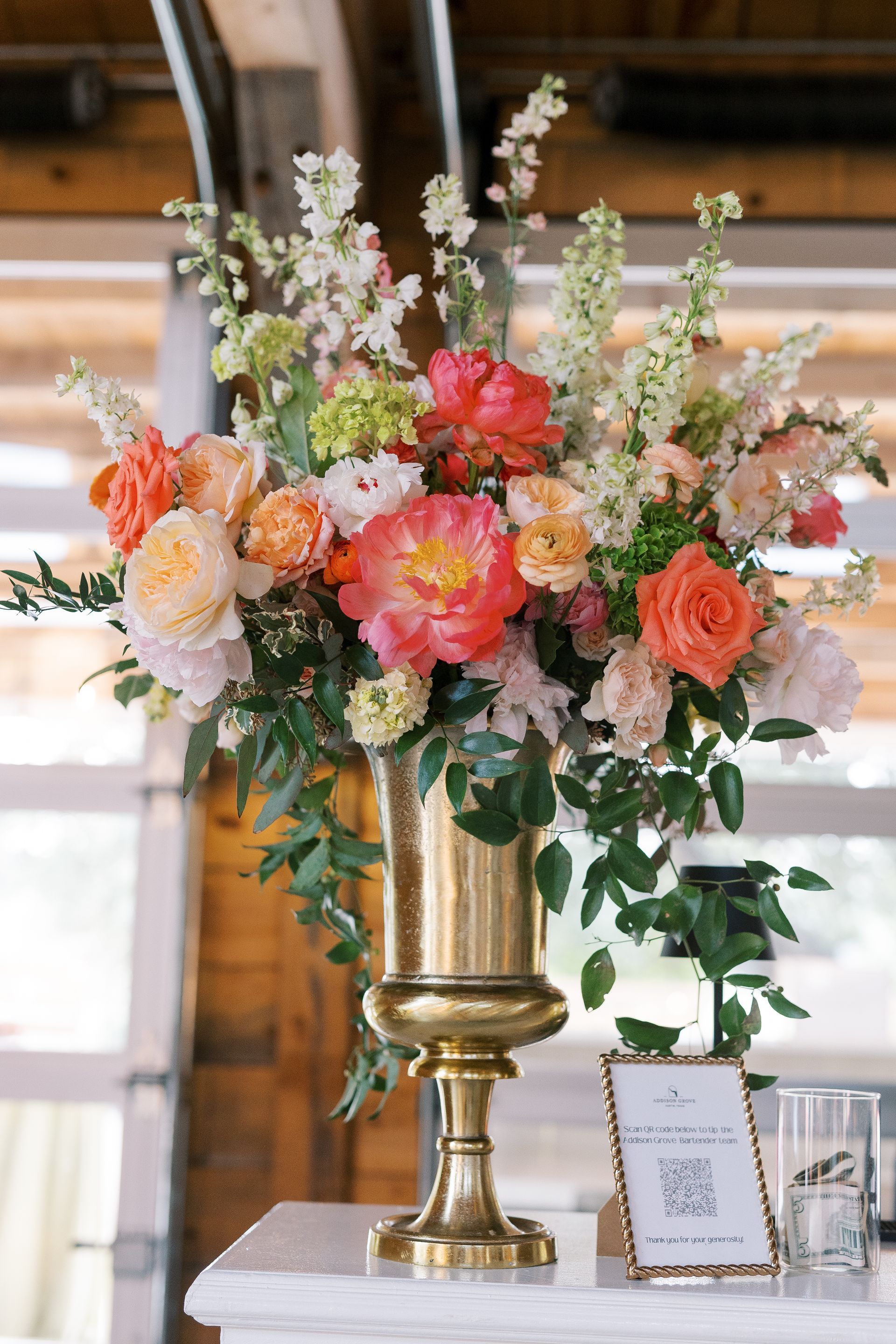 Floral arrangement with pink, peach, and white flowers in a gold vase on a table indoors
