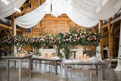 Elegant wedding reception setup in a barn with white drapes, floral arrangements, and candlelit tables