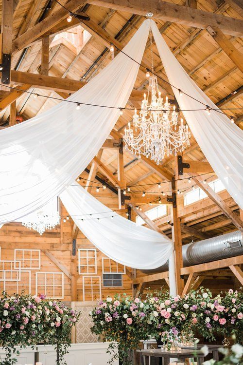 Wooden barn wedding venue with white drapery, crystal chandelier, and floral arrangements