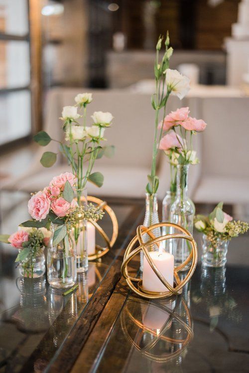 Elegant floral centerpieces in glass vases with gold geometric holders on a mirrored table