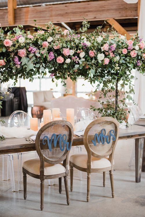 Floral wedding table with wooden chairs and pink-and-white flower arch in a rustic indoor venue