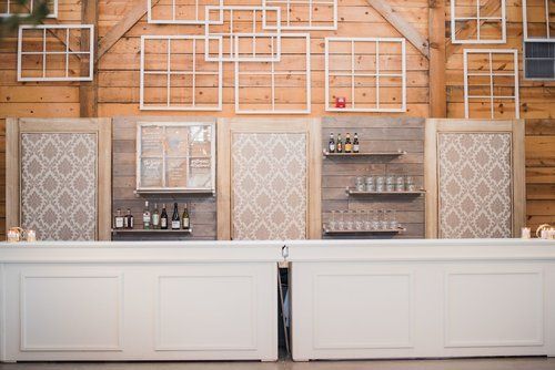 White bar with patterned wall panels and shelves against a wood backdrop, with bottles and glassware displayed.