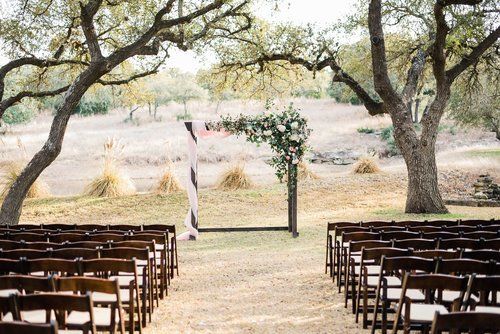Outdoor wedding ceremony setup with rows of chairs and a floral arch beneath trees