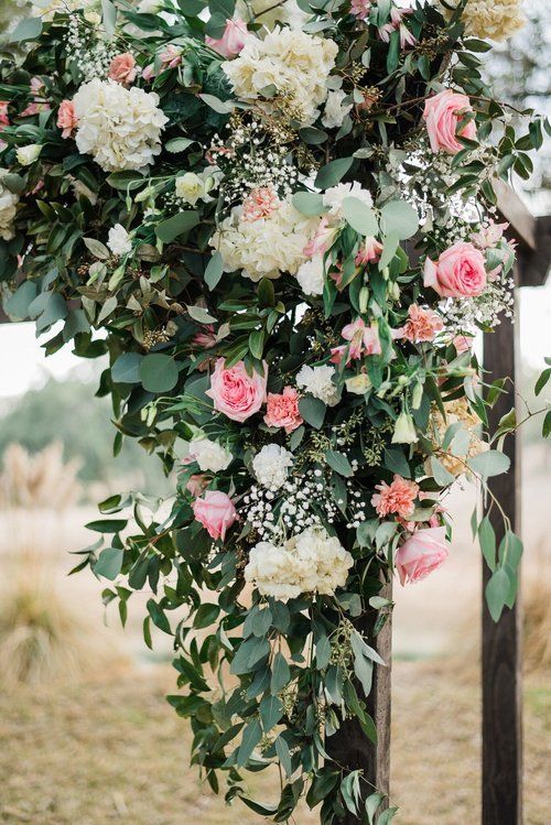 White and pink floral arrangement cascading over a wooden structure outdoors
