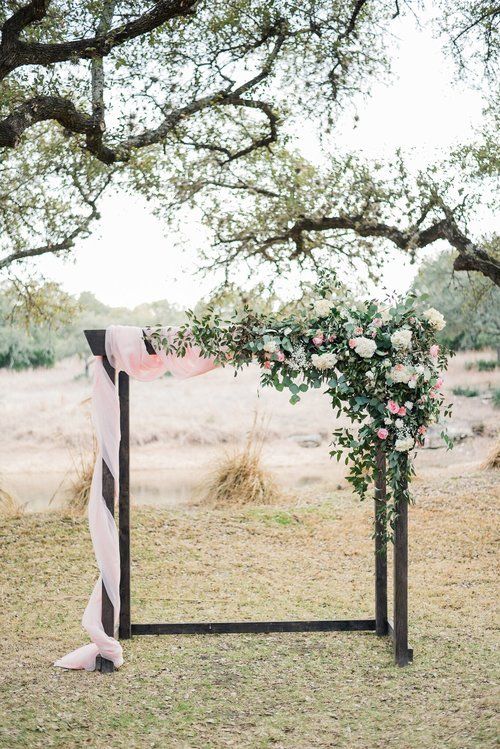 Floral arch with pink and white flowers in an outdoor field under trees