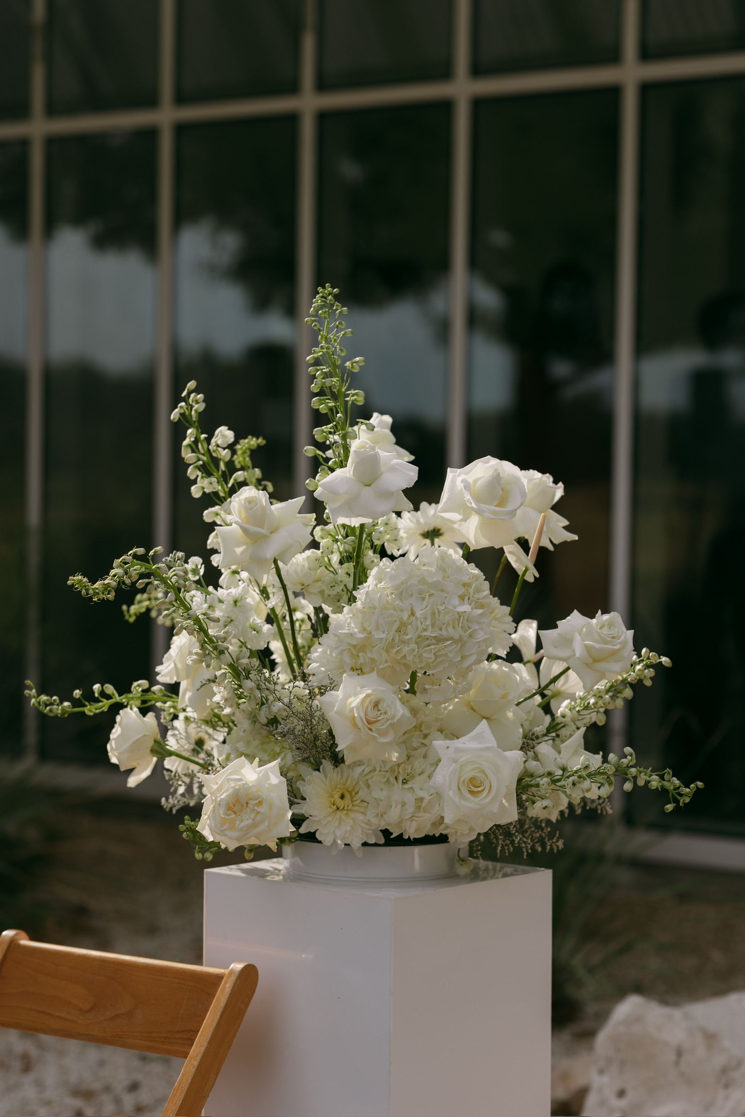 White floral arrangement in a tall vase on a table, with a blurred indoor background