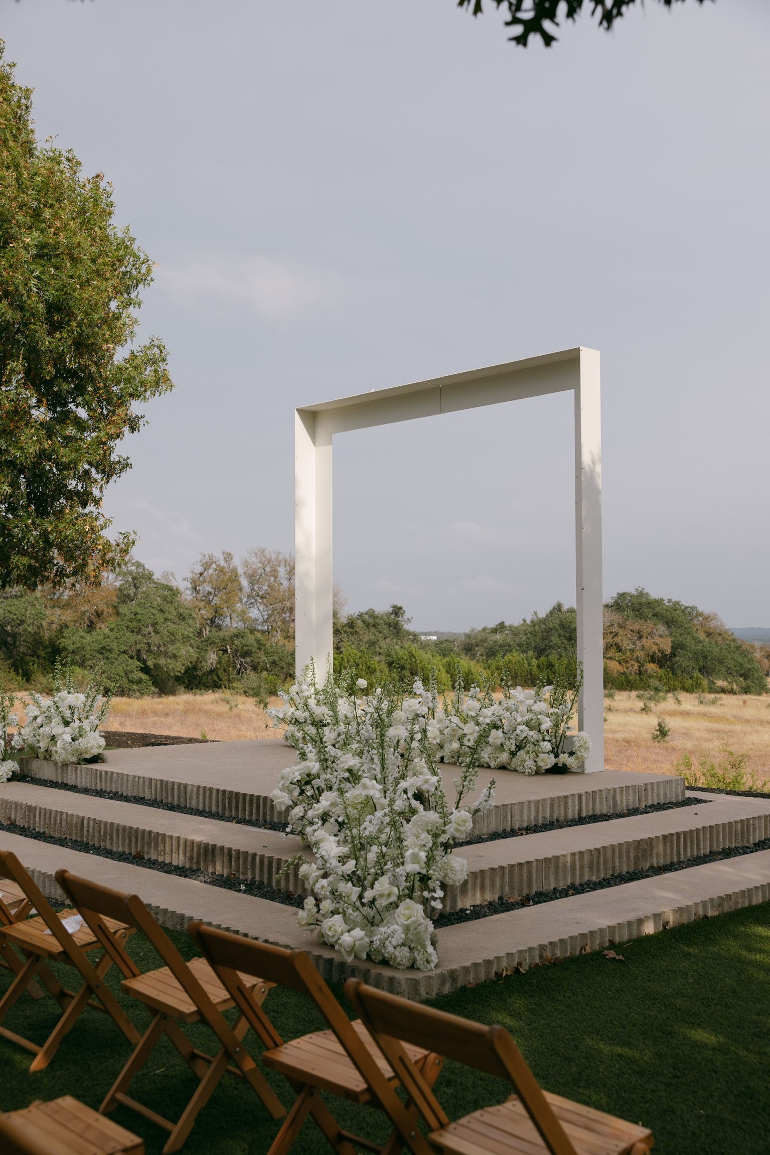 Outdoor wedding altar with white frame, wooden steps, and white flowers in a garden setting