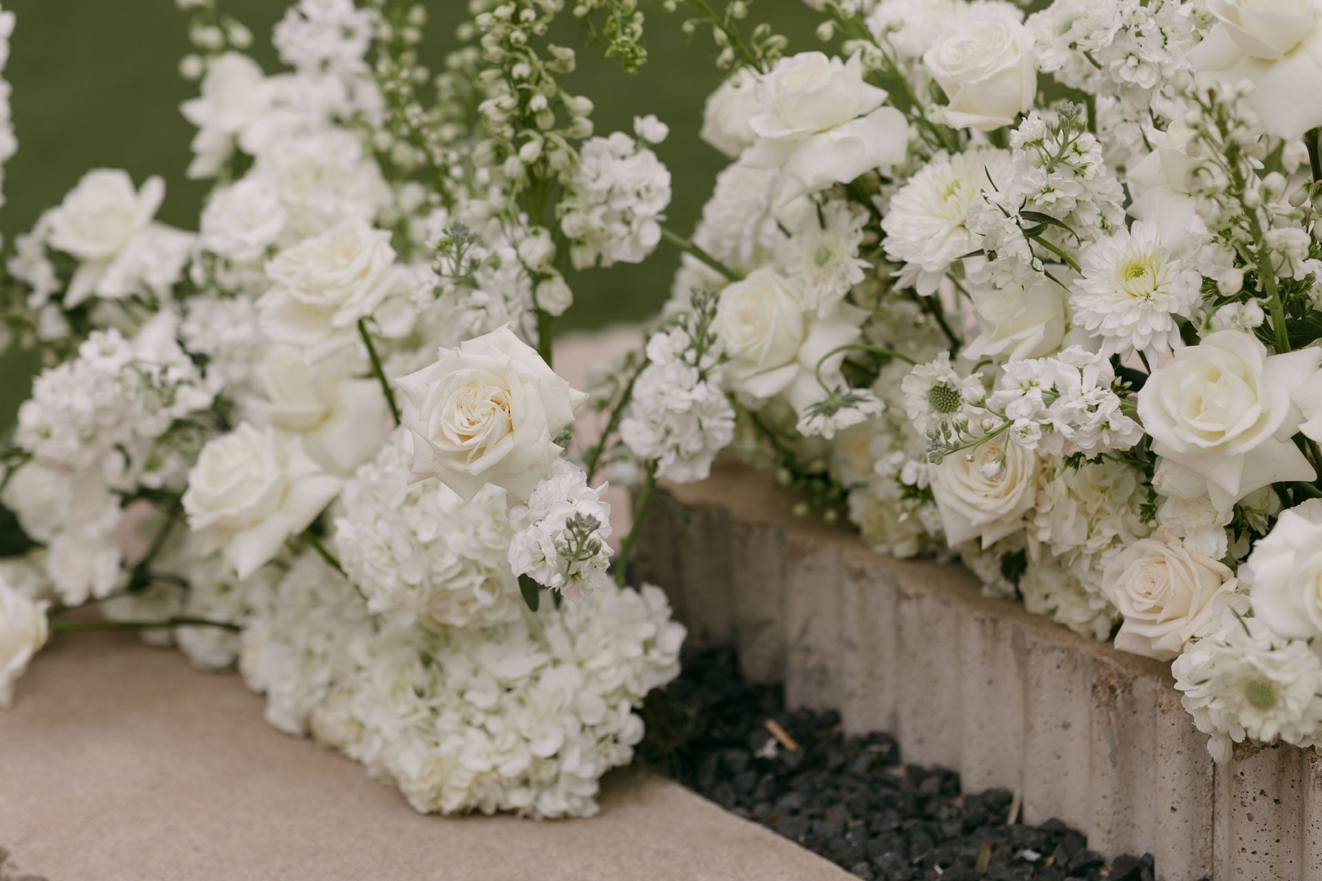White floral arrangements lining a stone step at an outdoor event