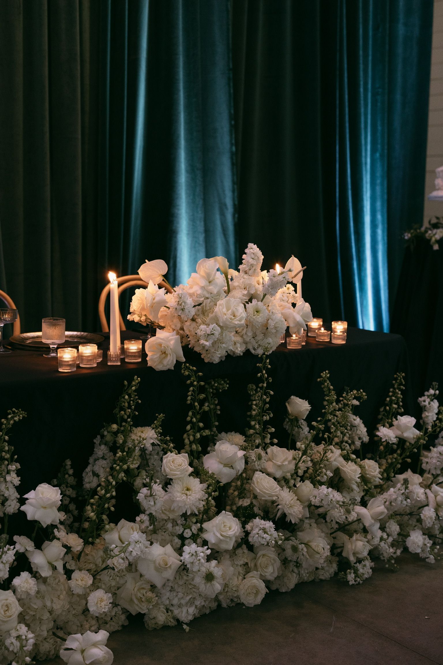 White floral arrangement with candles on a table before dark teal curtains