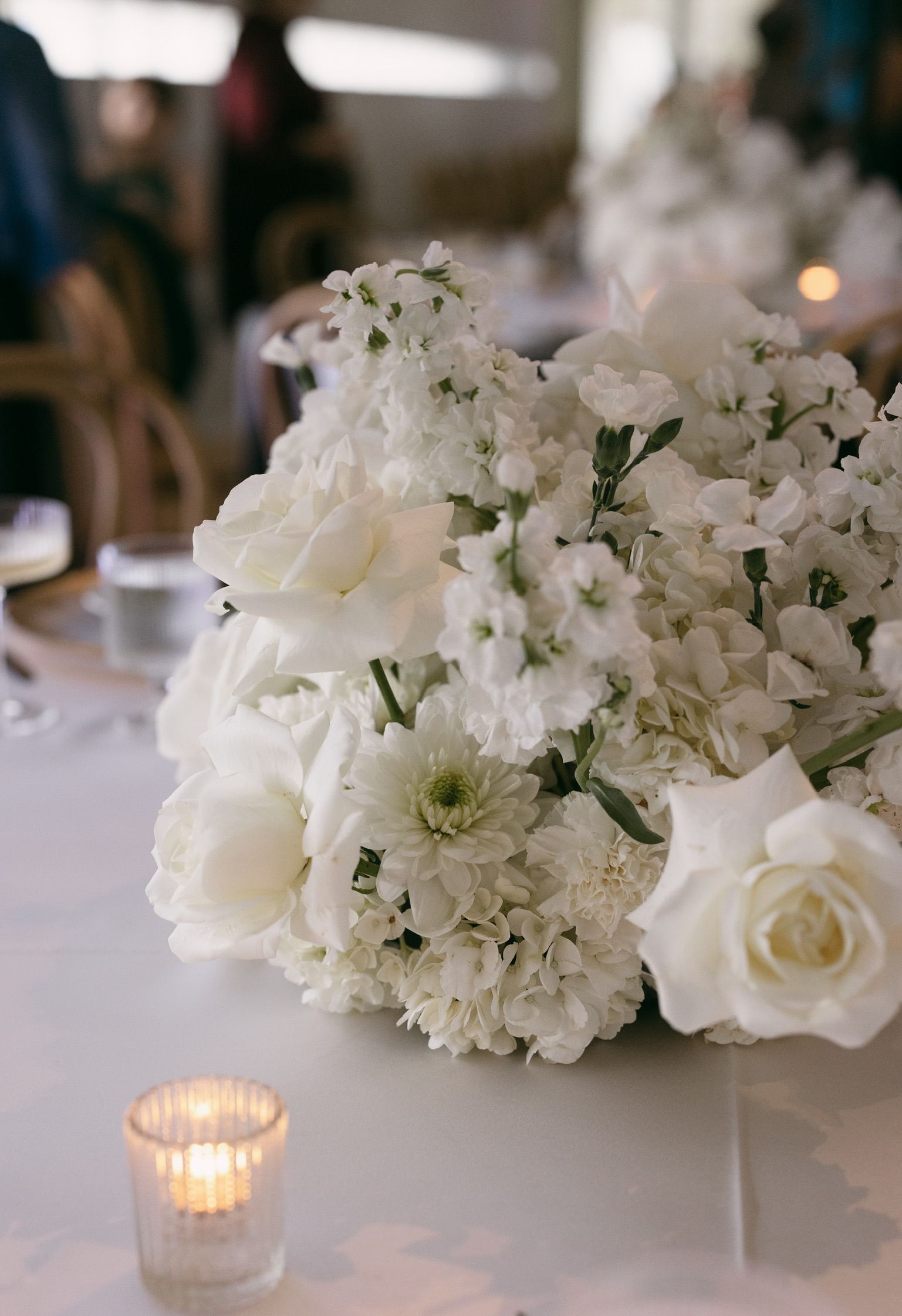 White floral centerpiece with roses and candles on a table at an elegant event
