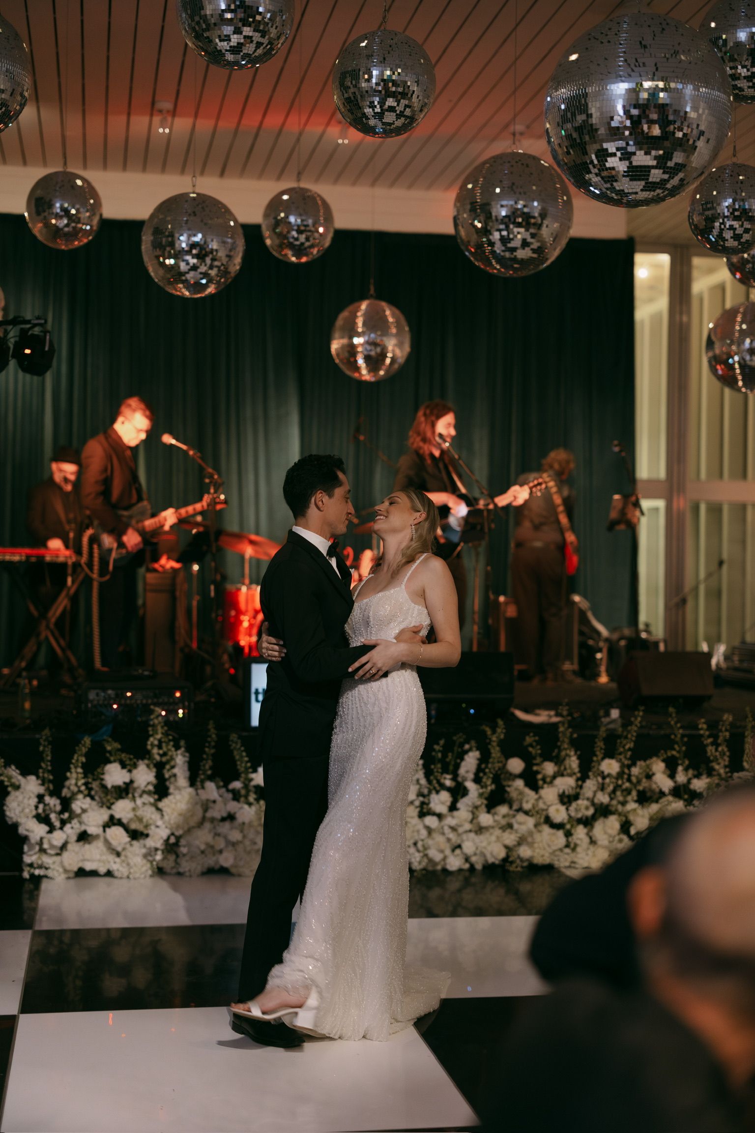Couple slow dancing at a wedding reception with a live band, disco balls, and black-and-white dance floor