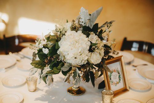 White floral centerpiece on a banquet table with candles, plates, and a framed place card