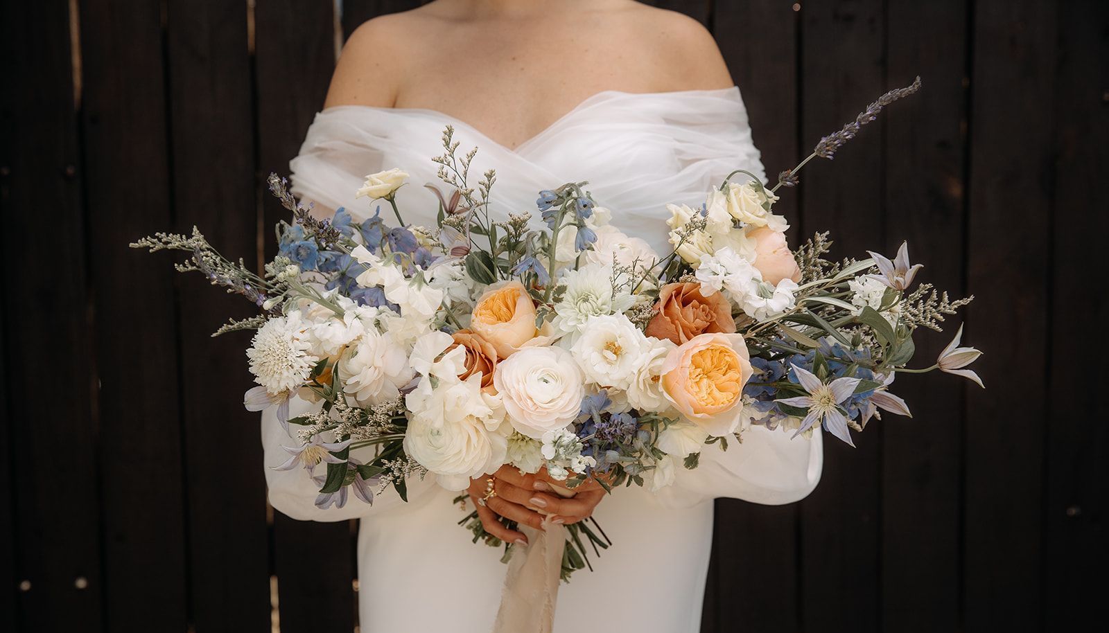 Bridal bouquet of white and peach flowers held against a white dress