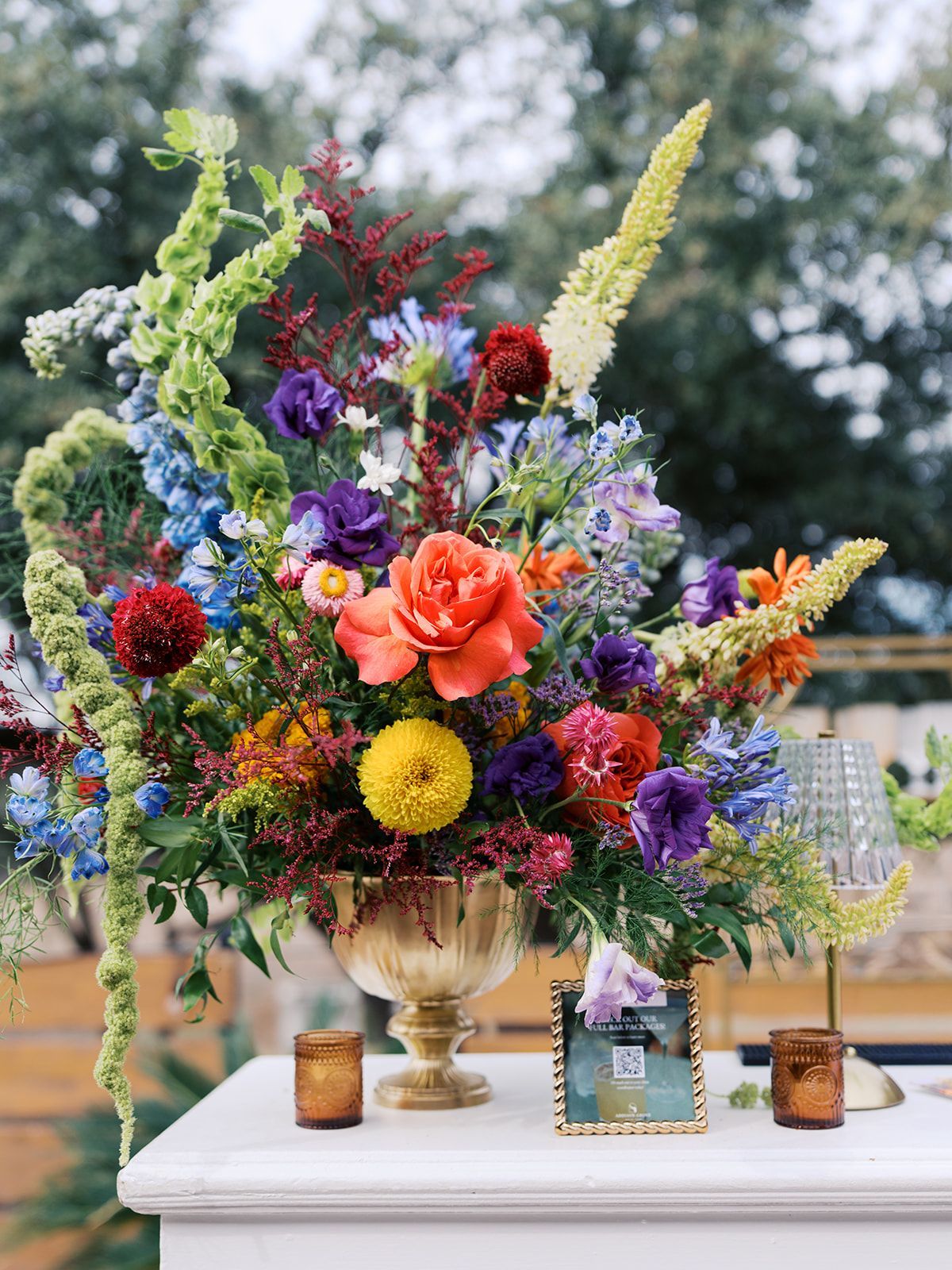 Colorful mixed floral arrangement in a gold vase on a white table outdoors