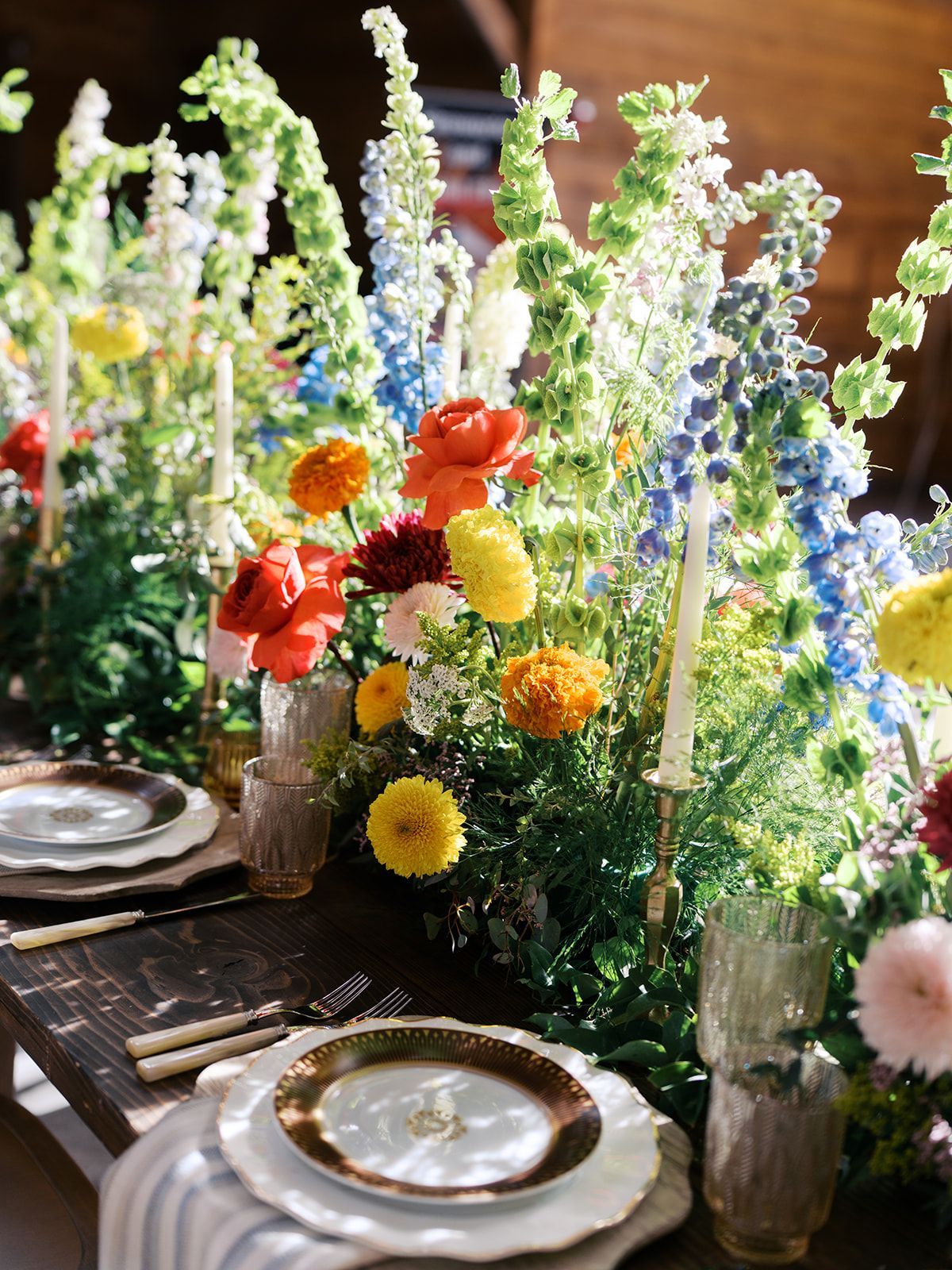 Colorful flower-filled table setting with plates, candles, and lush greenery in warm sunlight