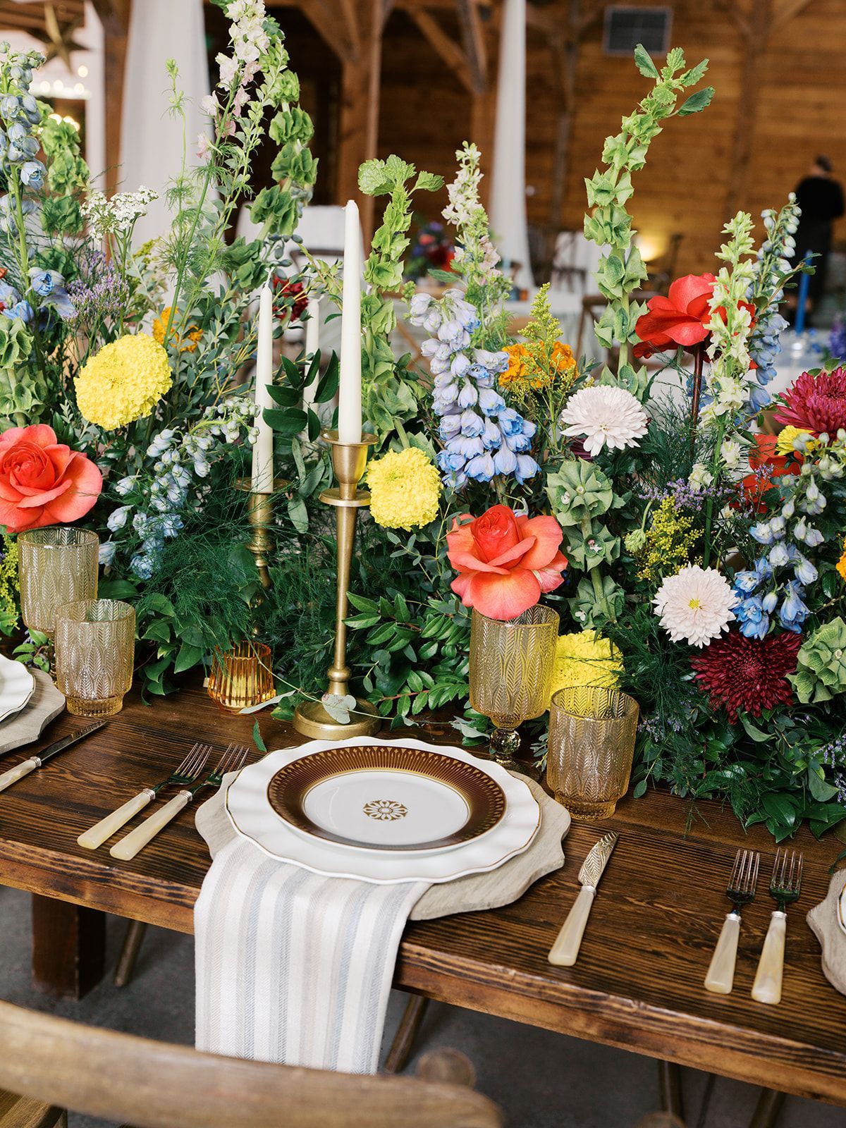 Elegant table setting with colorful floral centerpieces and gold candlesticks on a rustic wooden table