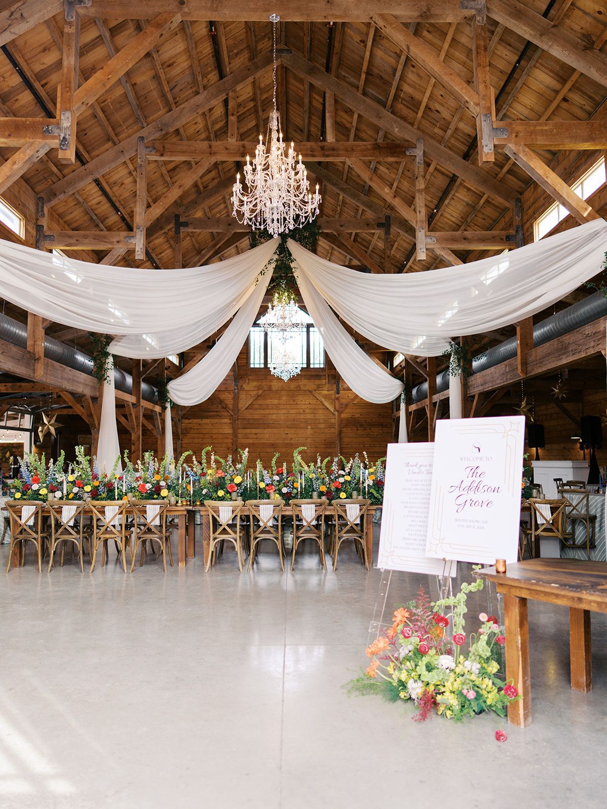 Rustic wedding reception hall with draped white fabric, chandelier, long table, and floral arrangements