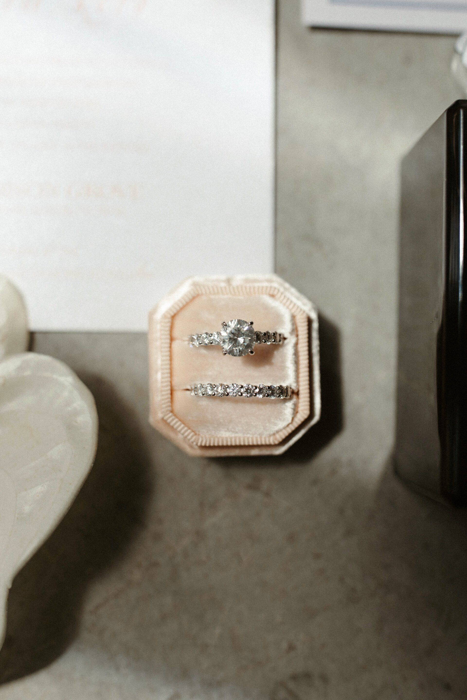 Small octagonal beige box with a silver bow on a gray surface, next to a dark rectangular object