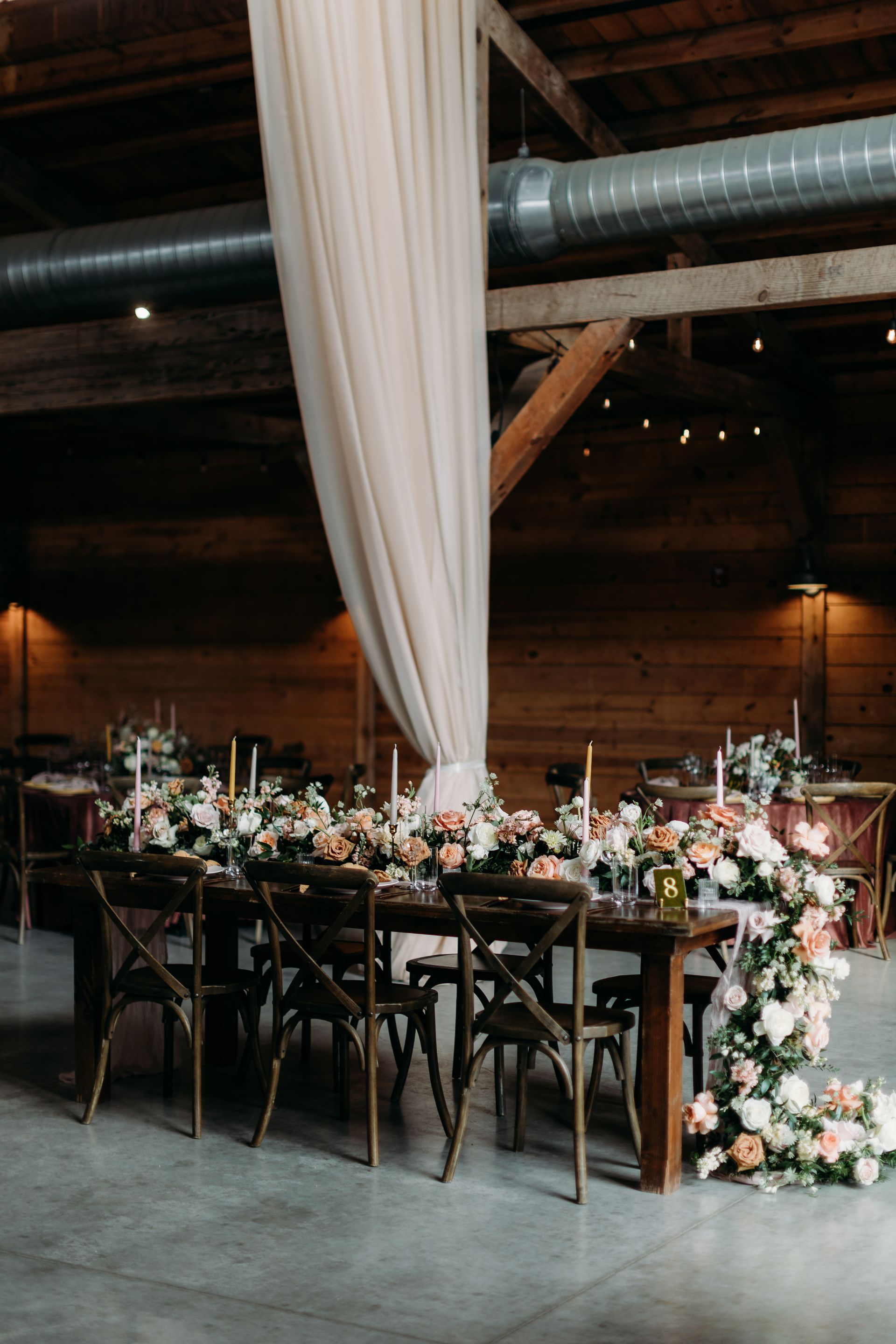 Elegant banquet table with white draped fabric and pink floral arrangements in a rustic hall