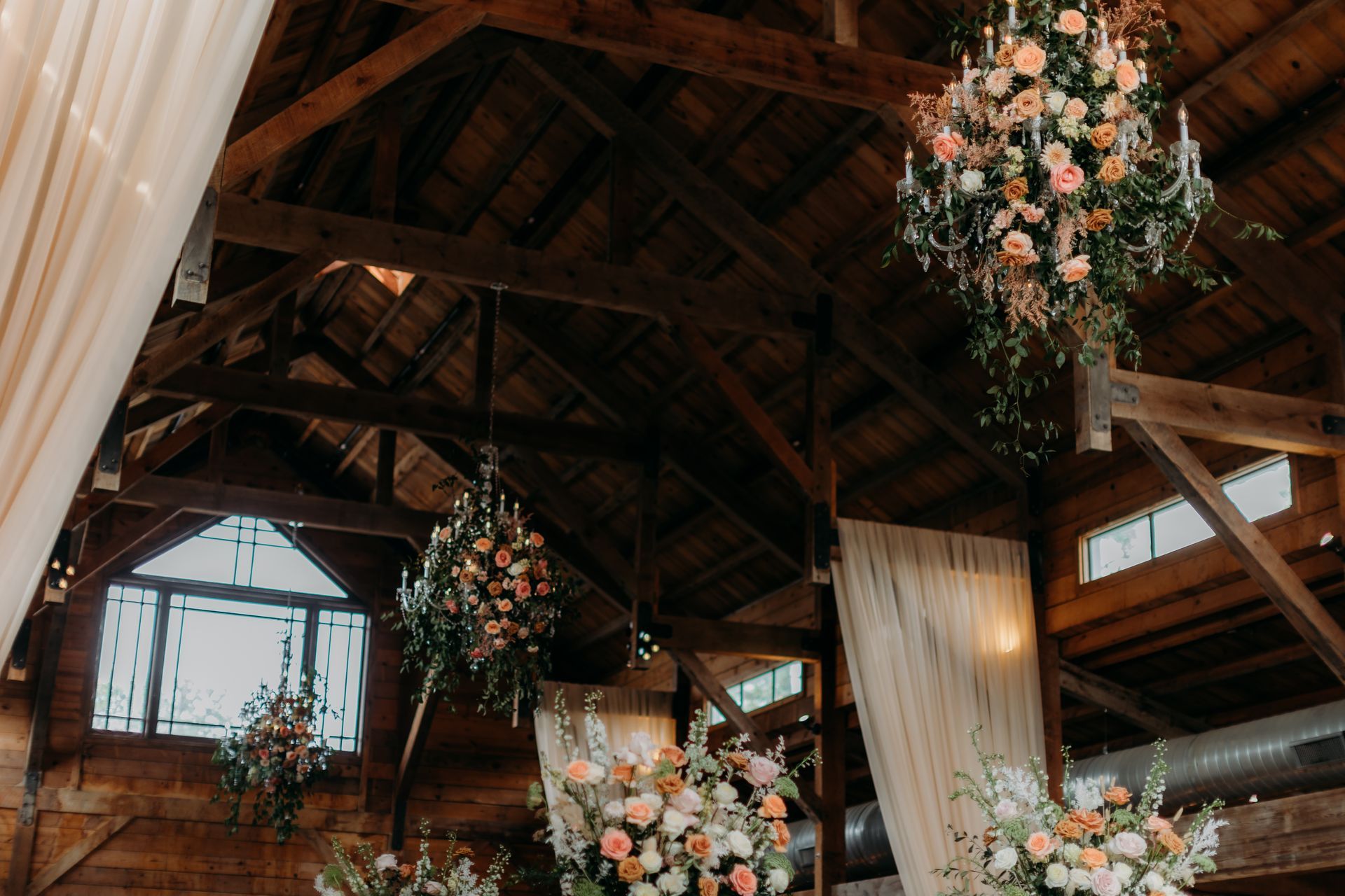 Rustic barn wedding venue with hanging floral chandeliers, draped fabric, and wooden beams