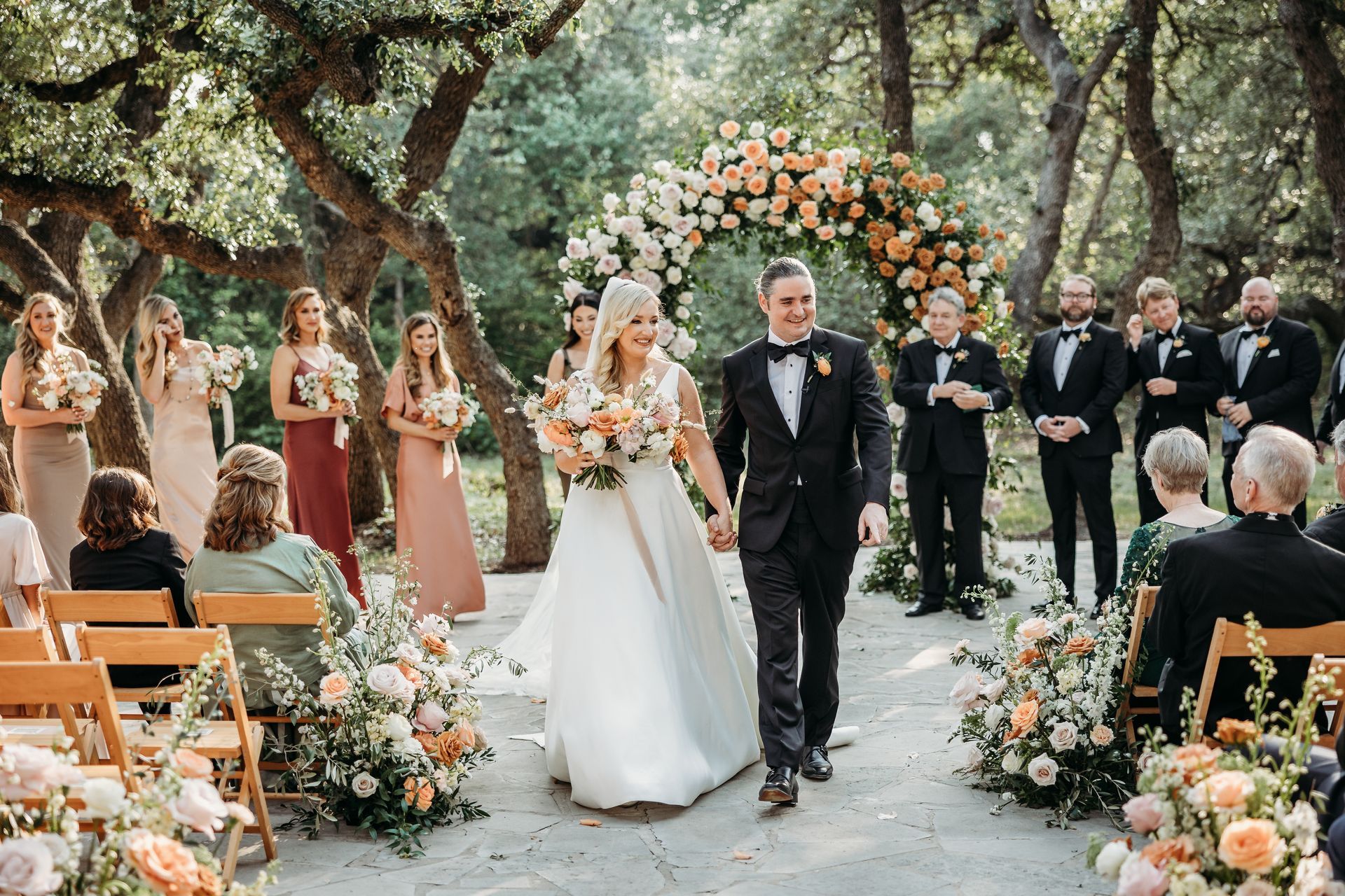 Bride and groom walking down an outdoor aisle at a flower-filled wedding ceremony