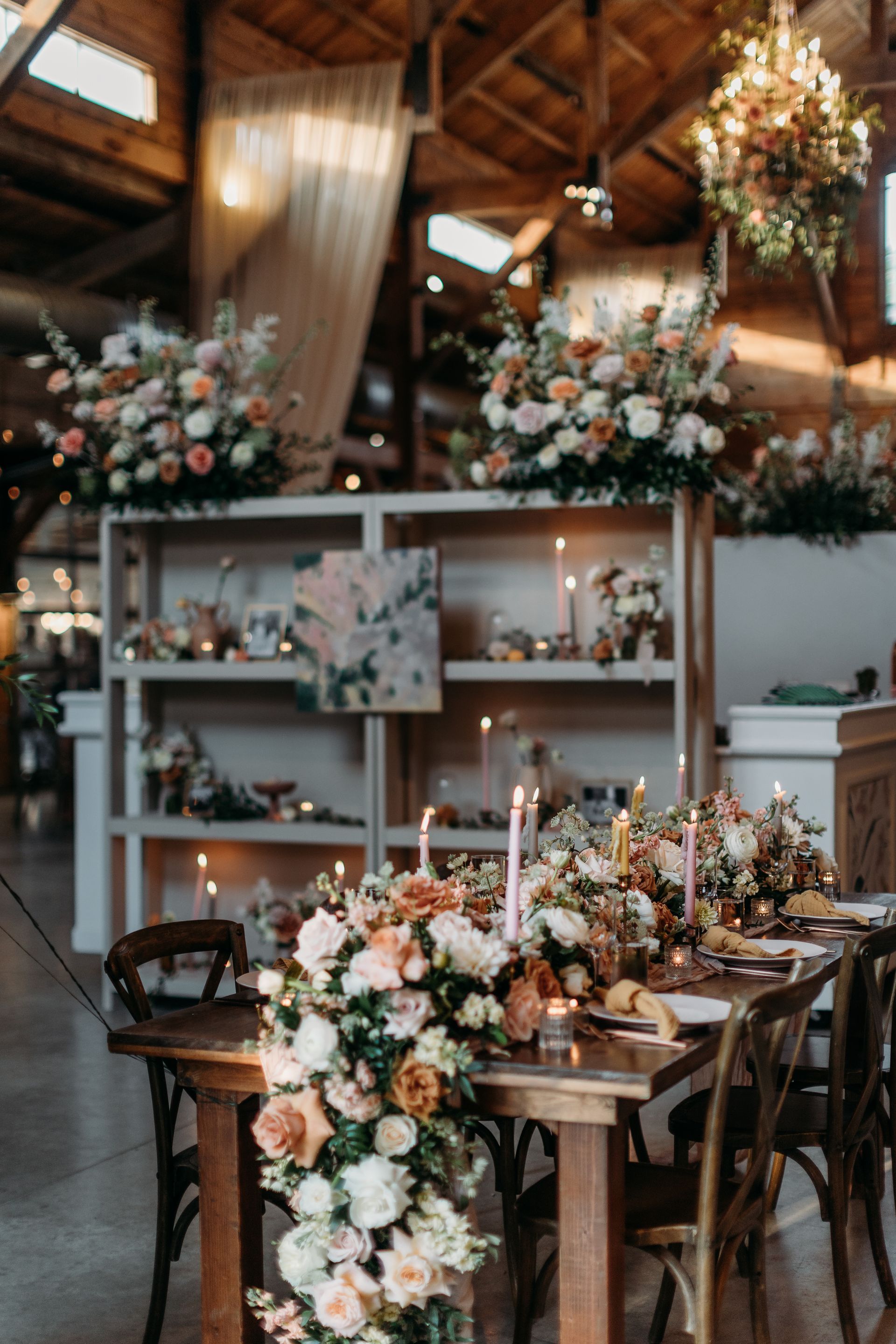 Elegant rustic wedding reception with floral centerpieces, candles, and wood decor in a warmly lit barn
