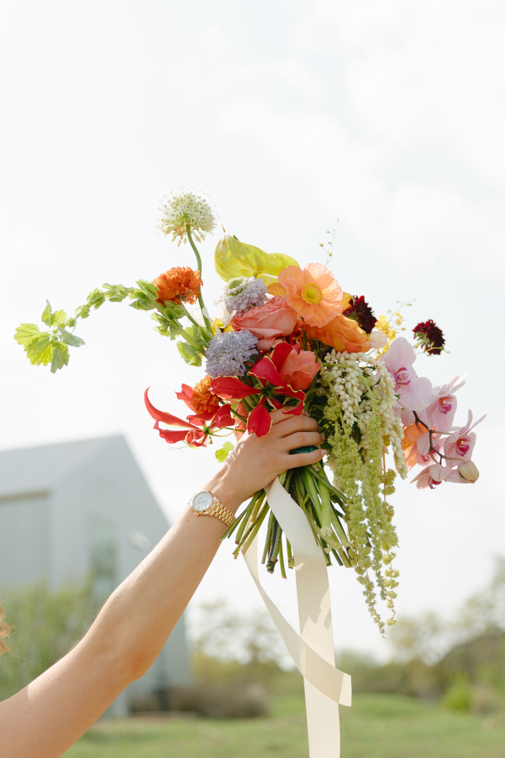 Hand holding a colorful wildflower bouquet outdoors against a bright sky