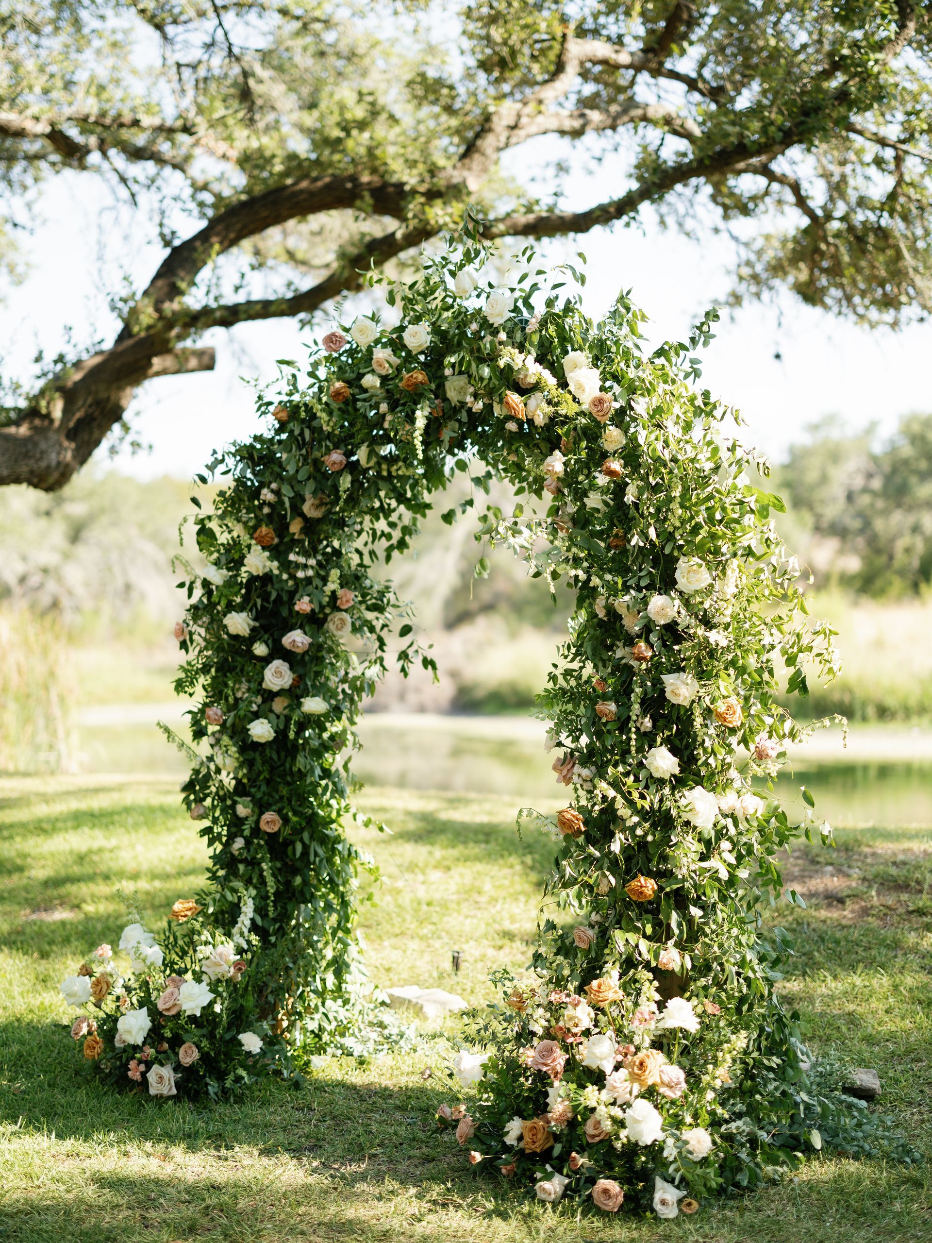 Flower-covered arch in a sunny garden, decorated with white and blush blooms and greenery.