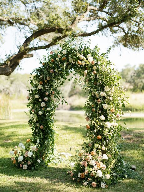 Flower-covered arch in a sunny garden, decorated with white and blush blooms and greenery.