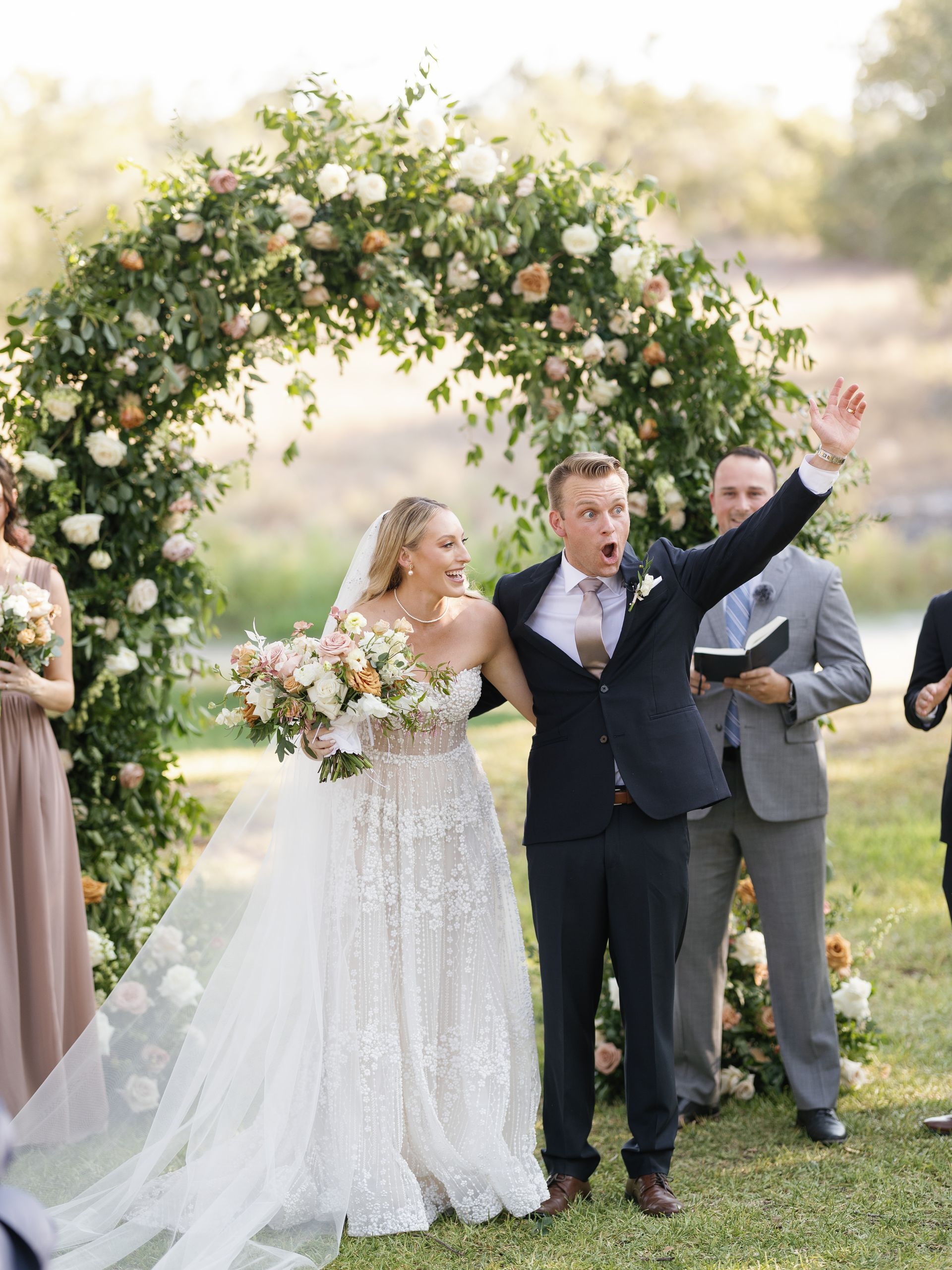 Bride and groom under a floral arch during an outdoor wedding ceremony