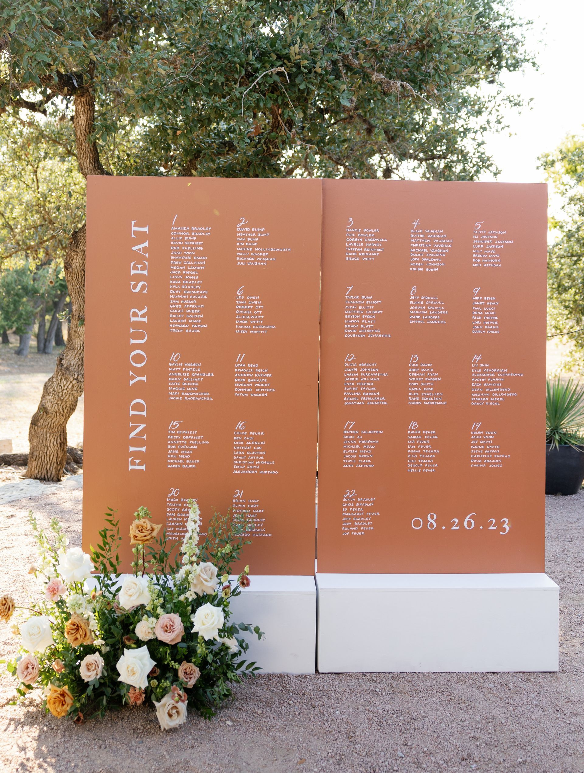 Rust-colored memorial wall with names and flowers at its base in a park