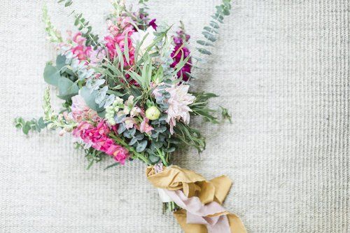 Pink and white floral bouquet with greenery, tied with a gold ribbon on a light textured background