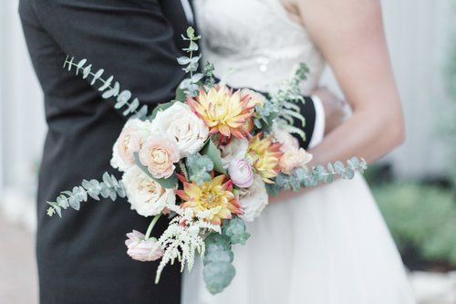Bride and groom holding a pastel floral bouquet in a soft outdoor setting