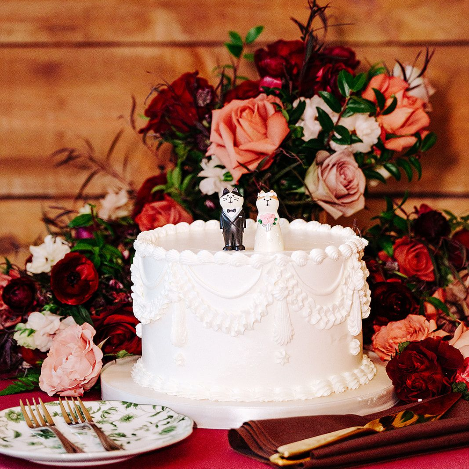 White wedding cake with red and pink flowers on a rustic wooden table