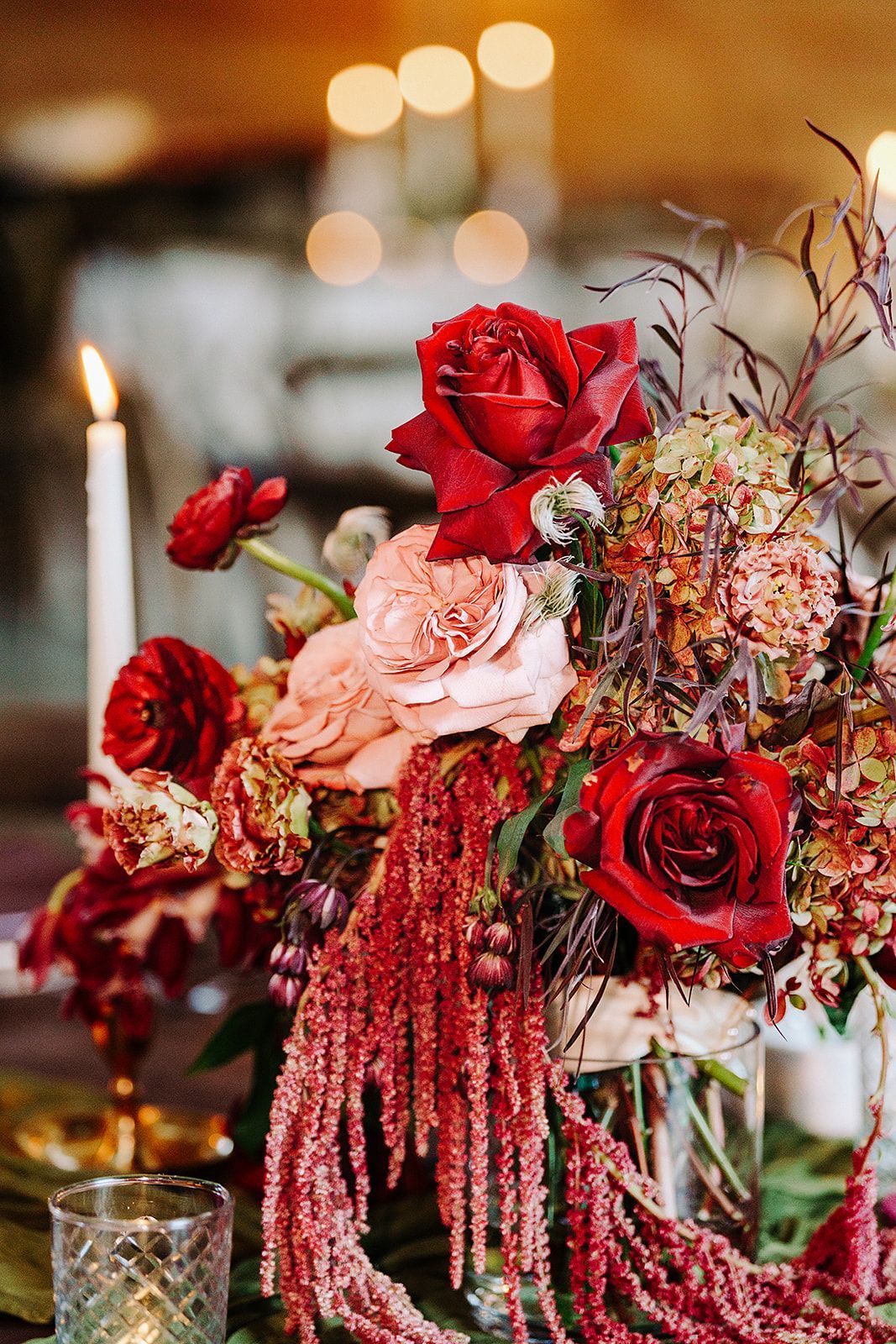 Red, pink, and cream floral arrangement with roses and hanging amaranthus on a decorated table