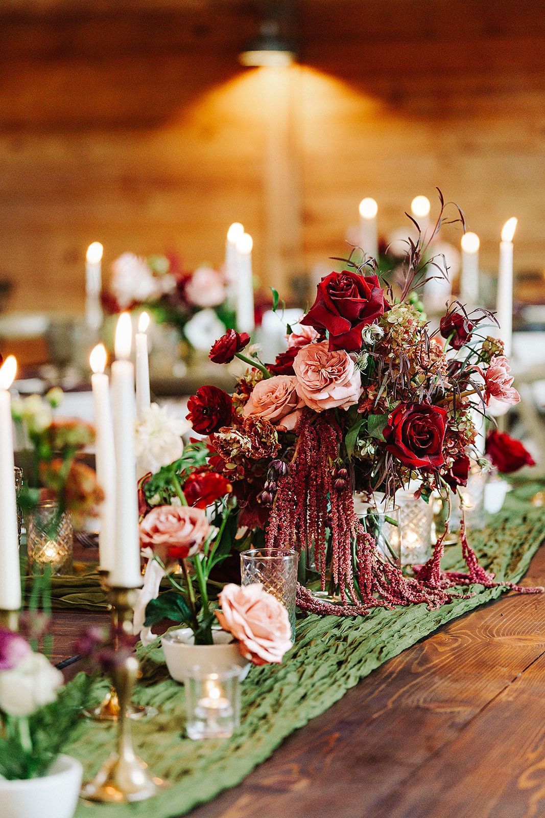 Elegant floral table centerpiece with candles and red flowers on a wooden table in warm indoor lighting