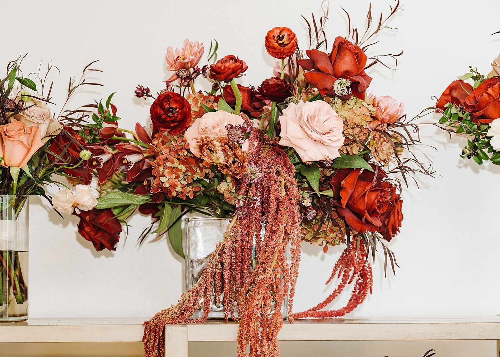 Floral arrangement of red, pink, and peach flowers cascading from a vase on a mantel.