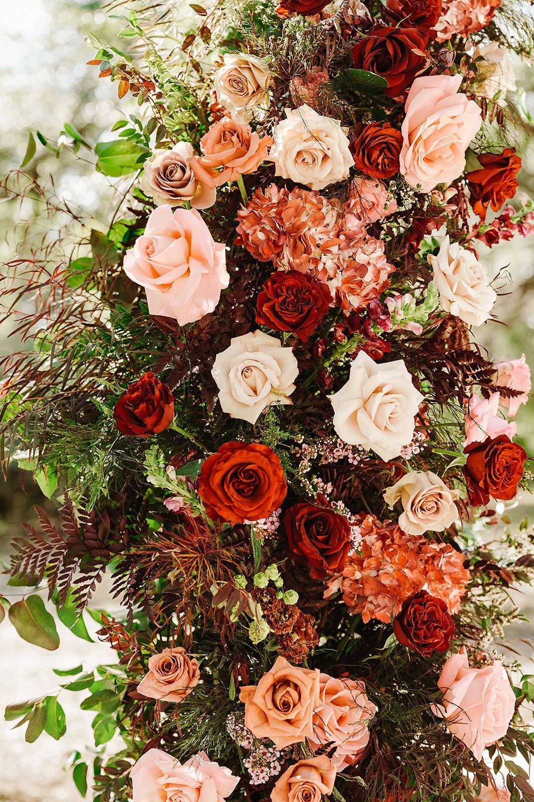Vertical floral arrangement with peach, cream, and deep red roses and greenery