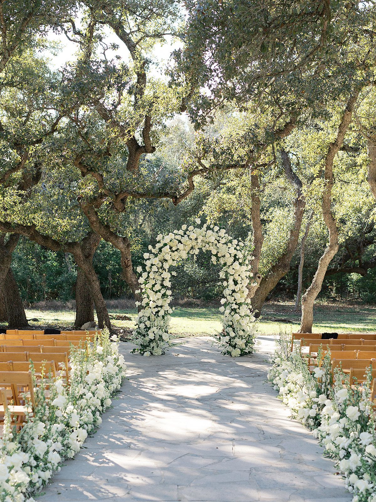 Flower-lined wedding aisle with a white floral arch under trees outdoors