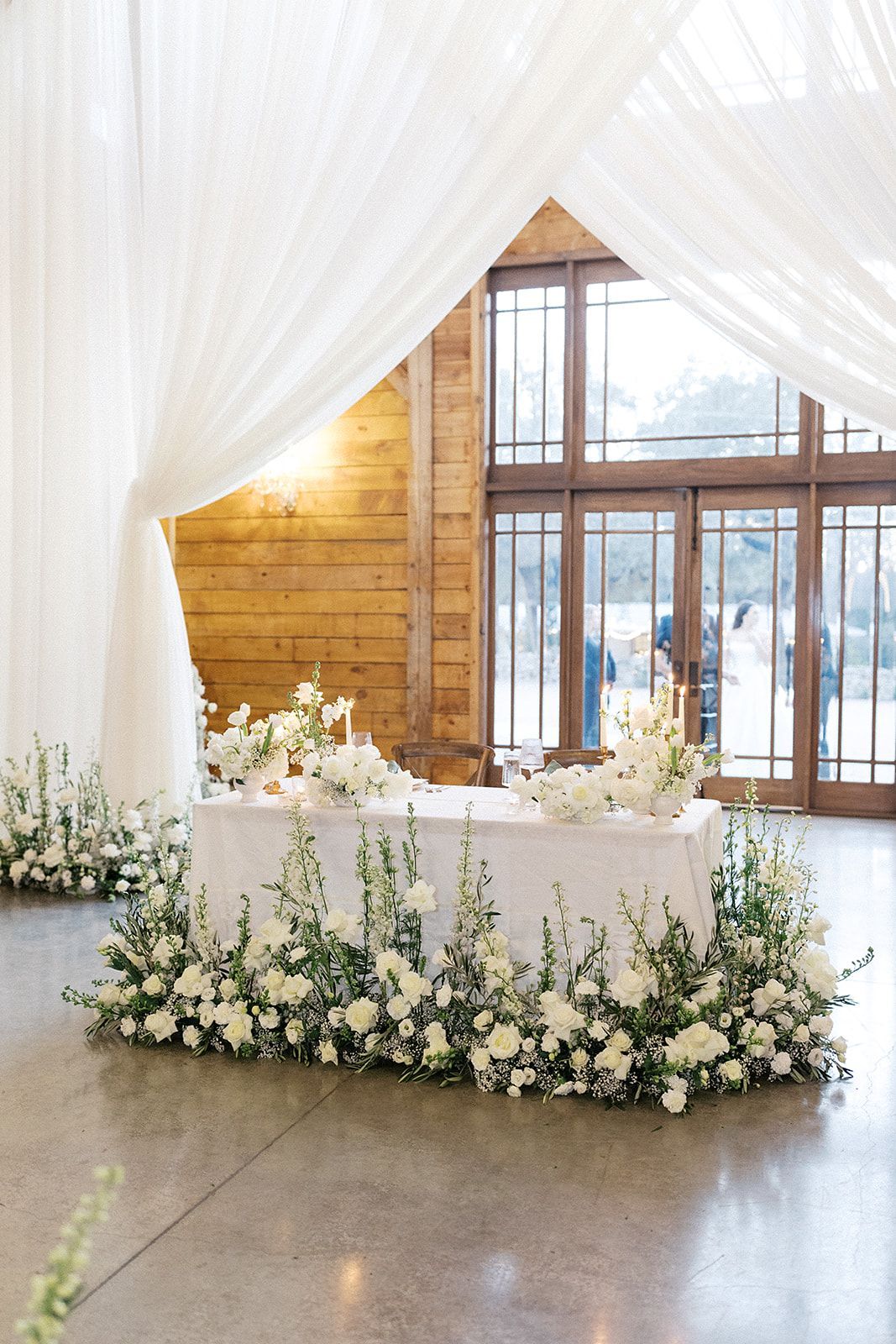 White floral wedding table with draped curtains in a bright rustic venue